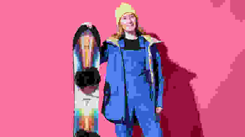 woman holding snowboard in front of pink background