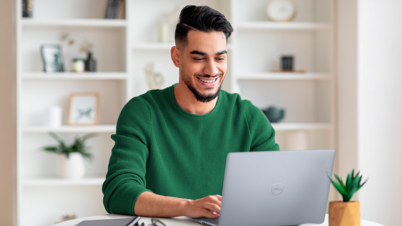 A man using a Dell Inspiron 14 Plus laptop at a white table.