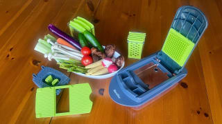 A bowl of assorted vegetables next to the Mueller Veggie Chopper and its attachments.
