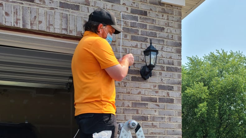 Person in orange shirt on ladder installing camera next to garage door