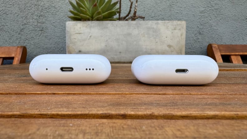 The two white AirPods Pro cases sit next to each other on a wooden table.
