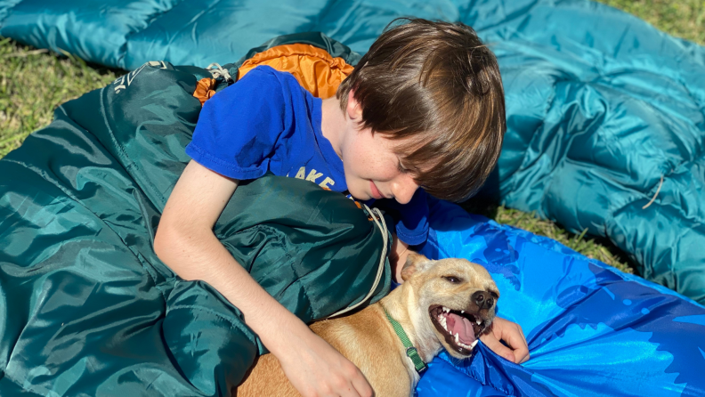 A child smiles in the Kelty Mistral bag with a dog smiling nearby