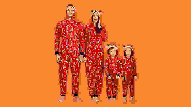 A family wearing the PatPat Red Reindeer matching Christmas onesies on an orange background.