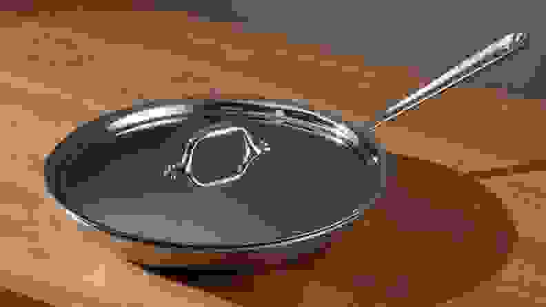 An All-Clad pan is photographed on a kitchen island with the lid on, its silver metal gleaming in the light.