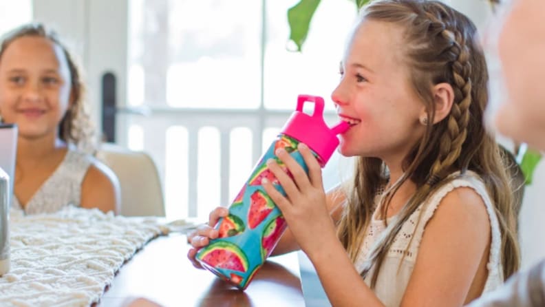 A girl smiles as she sips from a water bottle.