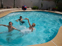 Three youths play pool basketball in an in-ground swimming pool.