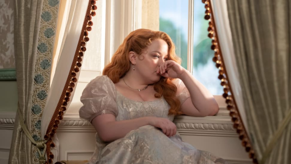 An image of Penelope Featherington in the Netflix series "Bridgerton." Penelope sits in a window seat, gazing wistfully outward.