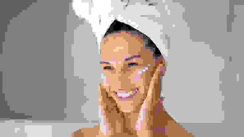 A woman applies moisturizer to her skin.