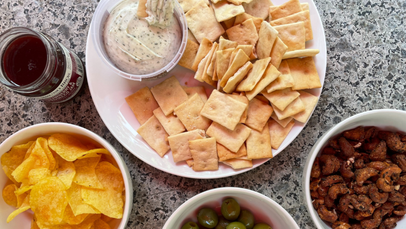 Bowls of chips, crackers, olives, and nuts sit on a counter.