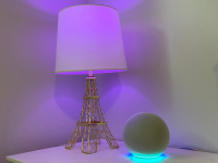 亚马逊(Amazon)的Echo Dot(第四代)放在白色床头柜上，旁边是一盏紫色智能灯泡。