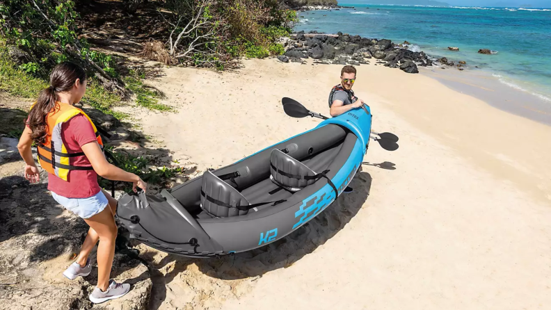 A couple on a beach carrying inflatable kayak.