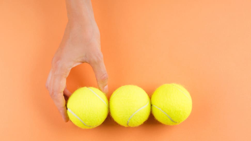 Hand touching three tennis balls on orange background.