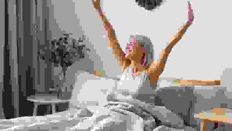 a person sits up in bed and stretches their arms