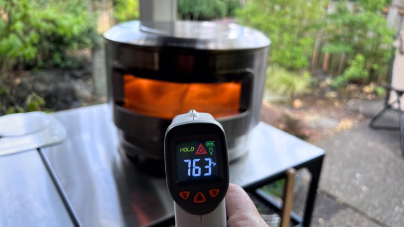 Person holding up thermometer in front of Solo Stove Pizza Oven.