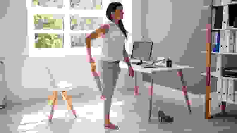 a woman stands in her home office and stretches on one leg