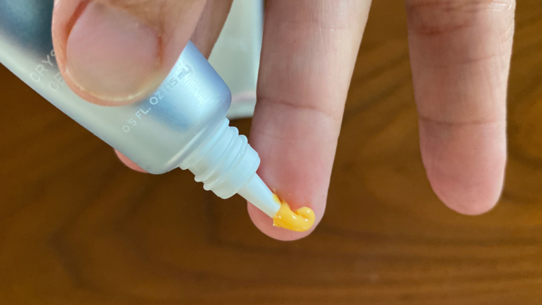 A person squeezes the eye serum on her finger. It's orange.