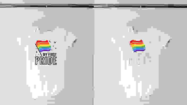Two white onesies hanging on a hanger with a rainbow flag on it and the words "My First Pride" written on it