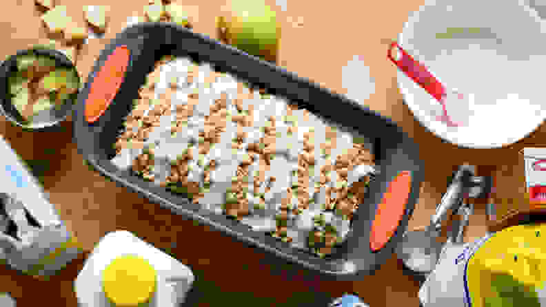 A Rachael Ray Yum-o! Nonstick Oven Lovin' Loaf Pan is in the center of a crowded kitchen counter. Inside the pan, there's a loaf of quick bread.