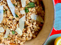 White beans, herbs, and shaved parmesan in a red Dutch oven.