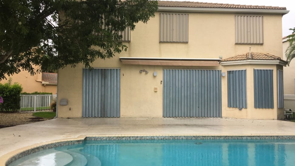 An in-ground pool in the backyard of a house with hurricane shutters