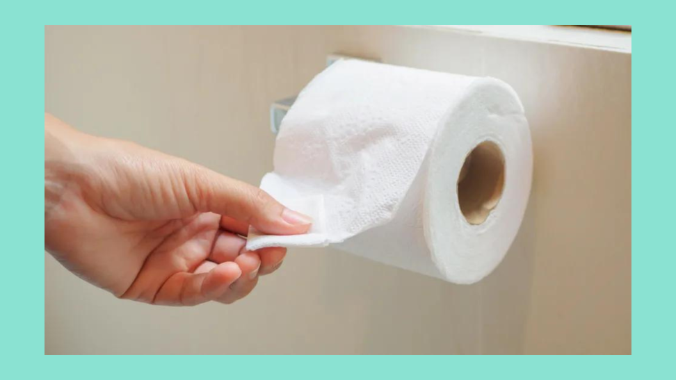 A hand pulls a sheet of toilet paper from a roll.