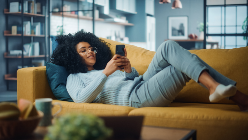 A person scrolls through their phone while sitting on a couch.