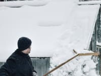 A man clears snow with a roof rake.