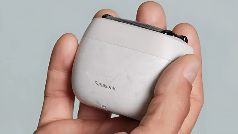 A hand holding a compact Panasonic electric shaver for men against a plain background.