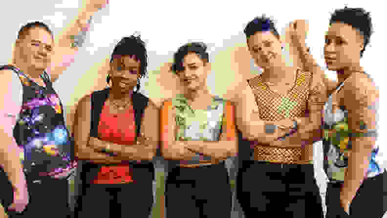 A group of people wearing binders of different patterns and designs, all wearing black pants, standing up against a wall.