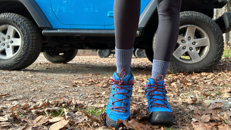 Close-up of someone wearing blue hiking boots in front of a blue Jeep.