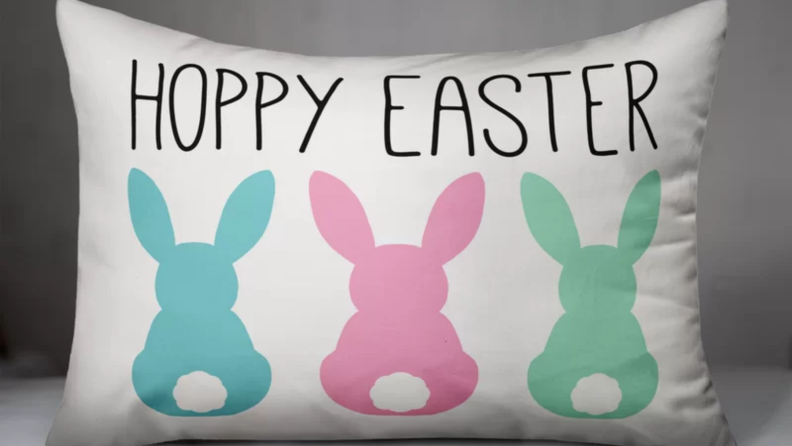 Three colorful bunnies on a white pillow that says Hoppy Easter