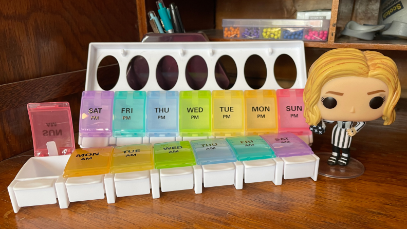 The Sukuos AM PM Weekly 7 Day Pill Organizer next to a Funko Pop figurine