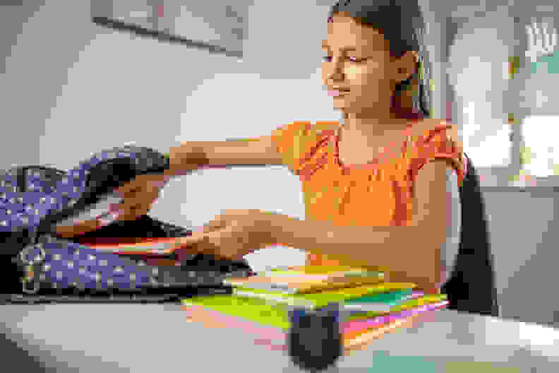 Girl packing her books in backpack after finished homework at home. She wears casual clothing and working in children's room.