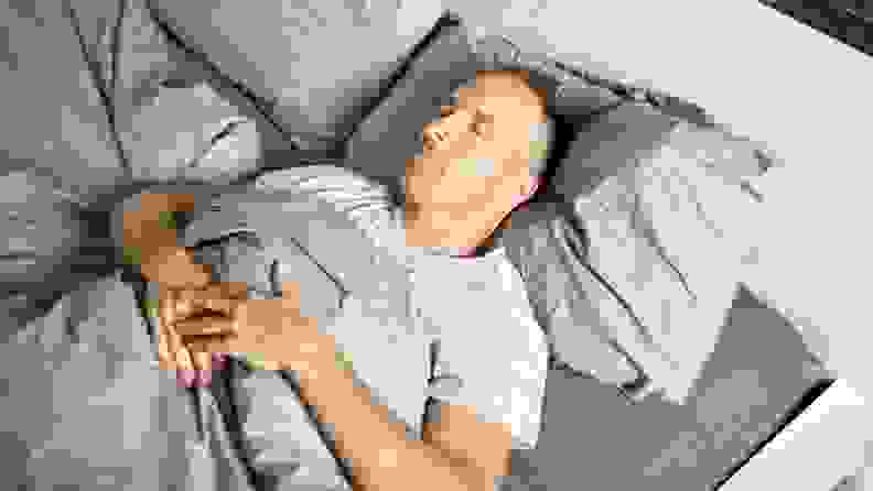 a person sleeps on their back in bed on gray sheets