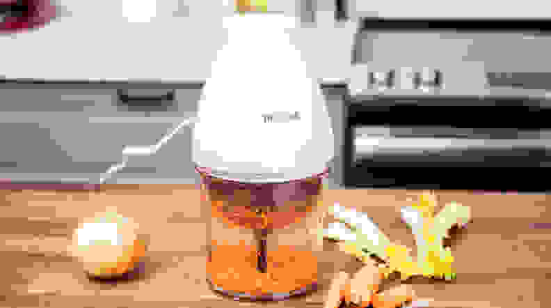 The Philips mini food processor is seen on a kitchen counter, with some onions, and other vegetables scattered around.