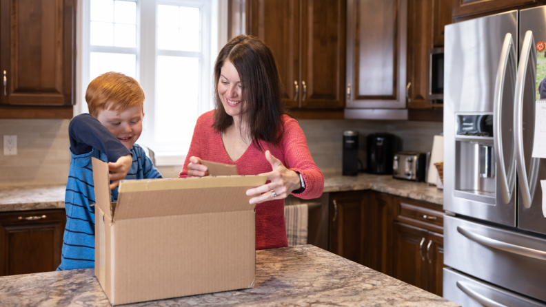 Mother and son in kitchen opening up package in kitchen.