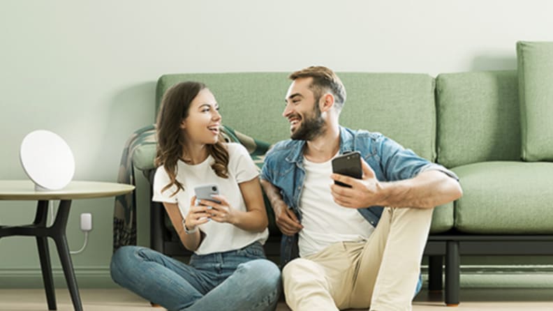 Two people sit next to each other on living room floor with light therapy lamp on nearby table.