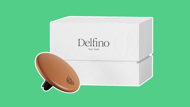 A round, brown Delfino car diffuser in front of a white box, on a green background.