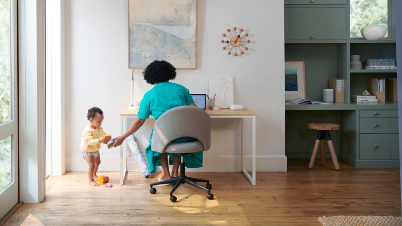 A woman hands a baby a toy as she works on her laptop