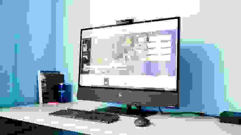 An image of the HP Envy all-in-one computer seen on a desk from the side with a blue wall behind it.