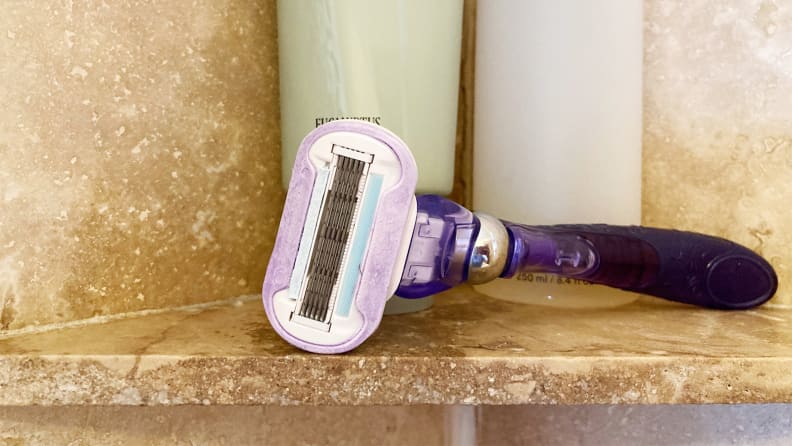 A purple razor sitting on the shelf in a shower.