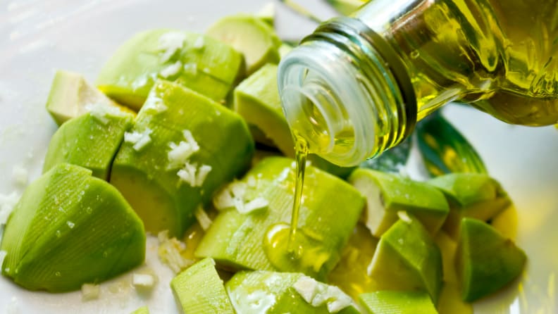 Someone pours olive oil on avocado salad.