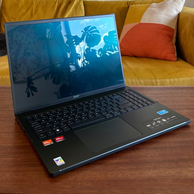 An open and powered off black laptop on a brown wooden surface with a mustard couch in the background