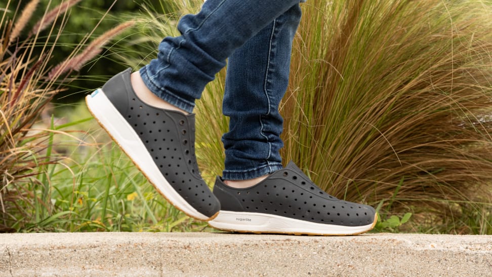 A child walks on a rock wall wearing Native shoes.