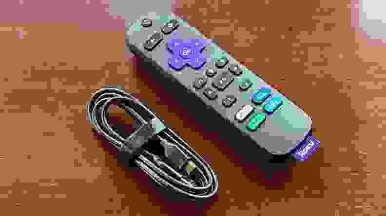 The black remote sits on a reddish brown table next to its cable in sunlight.