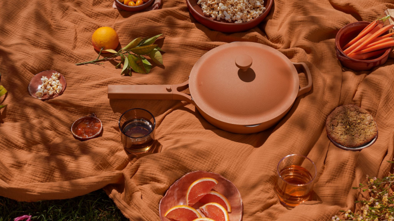 A terracotta-colored Always Pan is in the center of the image, with citrus fruits scattered all around.