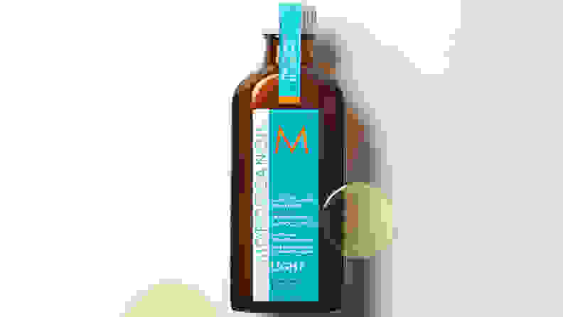 Bottle of moroccan oil with drops of oil on off-white background