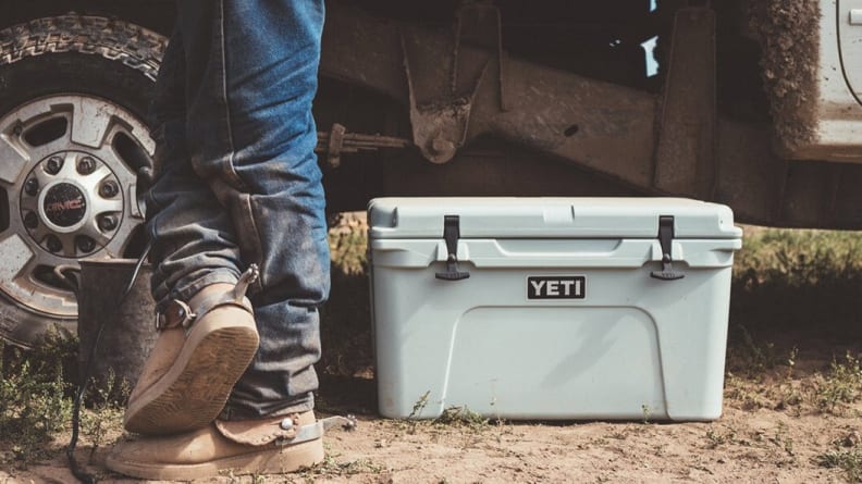 White colored cooler on ground next to man in jeans walking towards car.