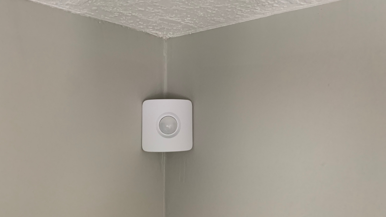 A SimpliSafe motion sensor hangs in the corner of a gray wall.