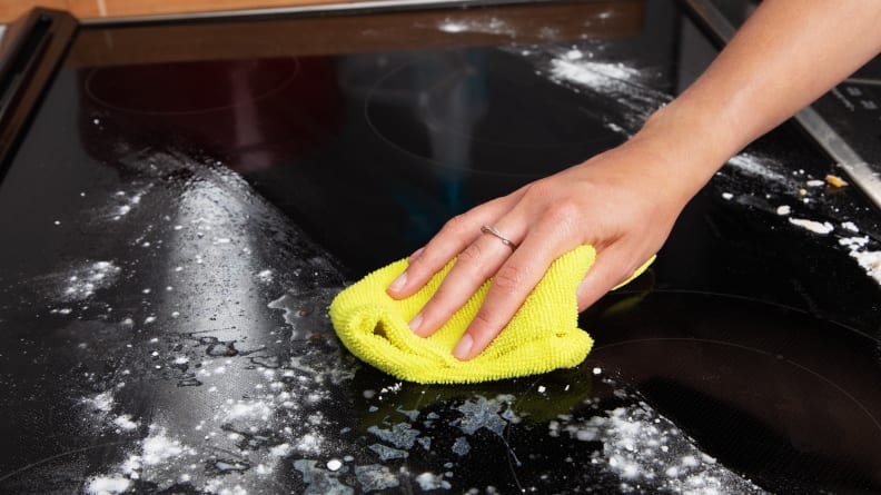 Eine Hand wischt eine saubere Linie auf eine Glaskeramikkochfläche, die mit Backpulver bedeckt ist.